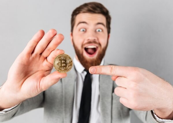 Close up a joyful of a cheerful businessman dressed in suit pointing finger at bitcoin isolated over gray background